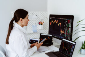 A photo of a woman sitting at her desk surrounded by multiple computer screens as she monitors various stock market charts.