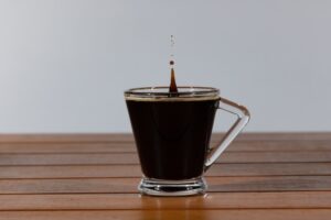 An isolated photo of the last drop of coffee falling into a glass coffee cup on a wooden table.