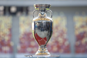 A photo of a silver tournament trophy with a blurred stadium in the background