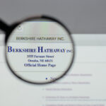 A photo of a magnifying glass held up to a computer screen showing the official Berkshire Hathaway logo at the top of the company’s webpage.