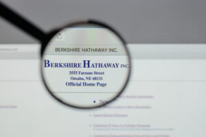 A photo of a magnifying glass held up to a computer screen showing the official Berkshire Hathaway logo at the top of the company’s webpage.