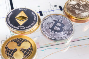 A photo of various crypto coins laid on top of a tablet showing a candlestick chart