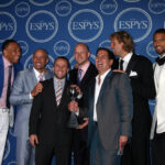 A photo of Mark Cuban holding a silver basketball trophy surrounded by players of the Dallas Mavericks at the 2011 ESPY Awards.