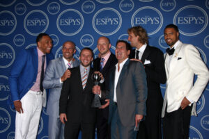 A photo of Mark Cuban holding a silver basketball trophy surrounded by players of the Dallas Mavericks at the 2011 ESPY Awards.