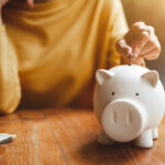 A photo of a woman’s hand putting a coin into a piggy bank.