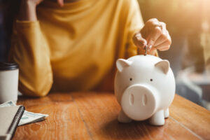 A photo of a woman’s hand putting a coin into a piggy bank.