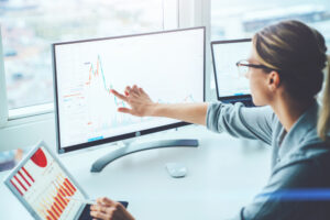 A photo of a businesswoman sitting at her desk analyzing financial graphs and statistics on her monitor.