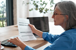 A photo of a woman holding a paper bill calculating her budget in her home office.