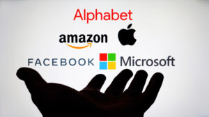 A photo concept of hand holding the logos of big tech’s big five: Alphabet, Facebook, Amazon, Apple, Microsoft.