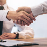 A close up photo of a handshake between a broker and a customer after signing contract documents.