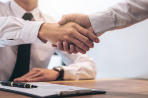 A close up photo of a handshake between a broker and a customer after signing contract documents.