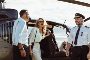 A photo of a couple laughing next to a pilot while stepping out of a private helicopter.