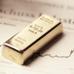 A photo of a bar of gold resting on top of a printed stock chart.