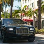 A black Rolls-Royce driving on the streets of Los Angeles, California, surrounded by palm trees.