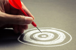 A hand placing a red dart in the bull’s-eye of a chalk-drawn dartboard.