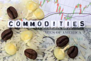 The word “commodities” is spelled out in letter cubes surrounded by coffee beans, corn and rice on top of a candlestick chart.