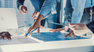 A close-up of a small group of engineers gathered around a conference table analyzing blueprints for a new design.