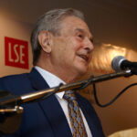 George Soros standing at the podium speaking into a microphone at the London School of Economics Alumni Dinner in Malaysia.