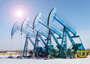 Four blue oil rigs line up next to one another at an industrial plant.