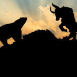 The silhouettes of a bear and a bull on the opposite sides of a mountaintop.
