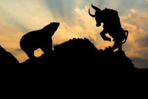 The silhouettes of a bear and a bull on the opposite sides of a mountaintop.