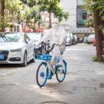 A person in a white hazmat suit rides a blue bicycle down a quiet street in Shanghai, China.