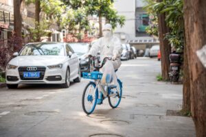 A person in a white hazmat suit rides a blue bicycle down a quiet street in Shanghai, China.