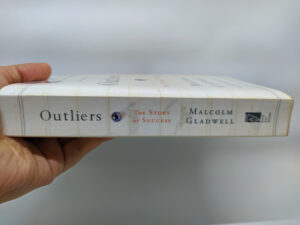 A hand holding Malcolm Gladwell’s book Outliers.