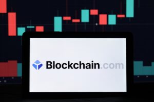 The blockchain logo on a white computer screen with a red and blue bar chart in the background.