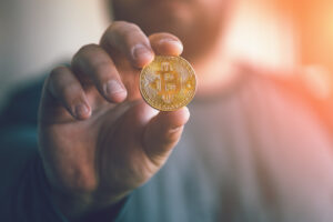 A man holding up a gold coin with the Bitcoin symbol on the face.