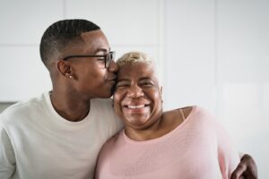 A mother and son embracing in the kitchen as he kisses her on the forehead and she smiles.