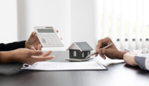 Close-up of two people’s hands as they discuss the terms of a home purchase agreement at an office table.