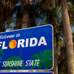 A blue highway sign that reads “Welcome to Florida The Sunshine State” in bold white letters.