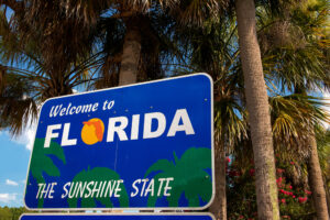 A blue highway sign that reads “Welcome to Florida The Sunshine State” in bold white letters.