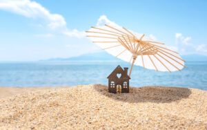 A tiny house shaded by an umbrella in the sand.