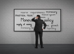 A businessman ponders monetary policy in front of a chalkboard.