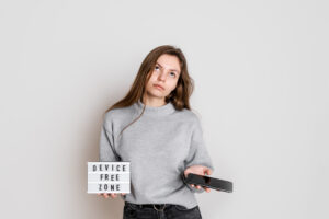 A girl holding a sign that says “Device-Free Zone” and a phone.