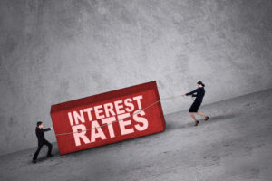 Two people with a rope dragging a brick that reads “interest rates.”