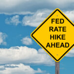 A sign warning of rate hikes against a blue cloudy sky.