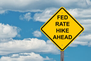 A sign warning of rate hikes against a blue cloudy sky.