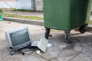 Old electronics in a pile next to the trash