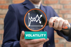 A man holding a magnifying glass that reads “volatility” under market trend lines.