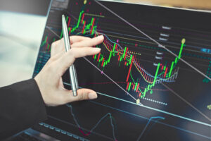 A hand traces the pattern of a technical analysis chart on a laptop screen.