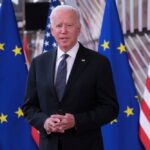 Joe Biden stands in front of the United States and European Union flags.