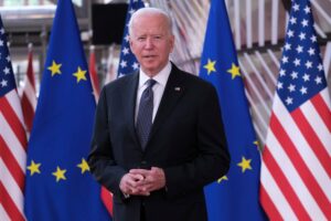 Joe Biden stands in front of the United States and European Union flags.