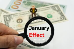 A magnifying glass reading “January effect” with a figurine standing over a dollar-bill.