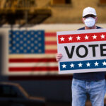 A man wearing a mask holding a sign that reads "VOTE."