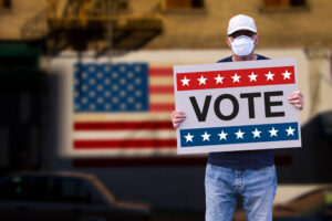 A man wearing a mask holding a sign that reads "VOTE."