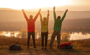 A trio of friends with their hands in the air looking at a mountaintop.