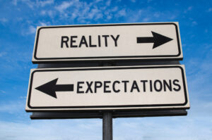 Two signs that read “reality” and “expectations,” respectively, with arrows pointing in opposite directions.